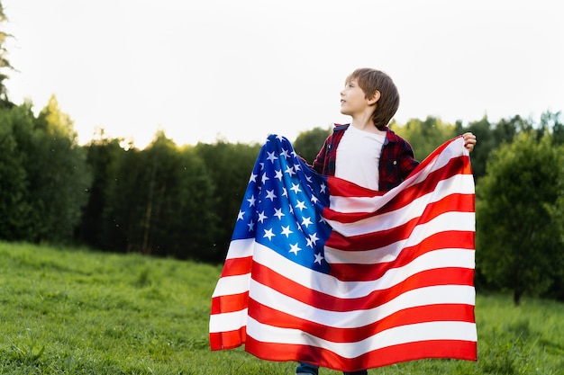 Mały chłopiec z amerykańską flagą w przyrodzie, pojęciem patriotyzmu i niepodległości USA.