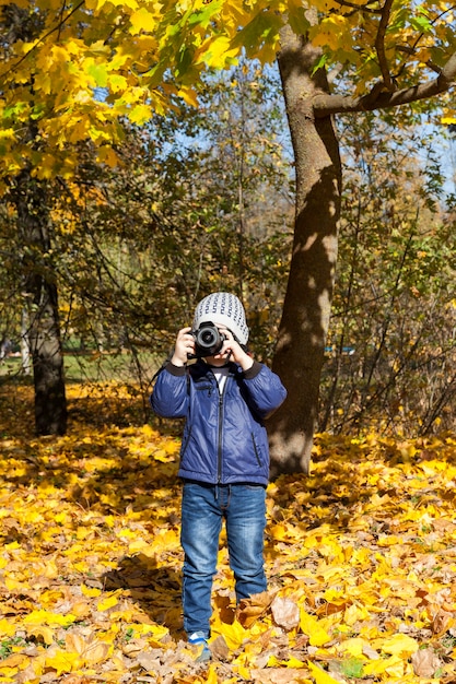 Mały chłopiec z aparatem fotograficznym, patrząc prosto w obiektyw, portret w jesiennym parku z bliska.