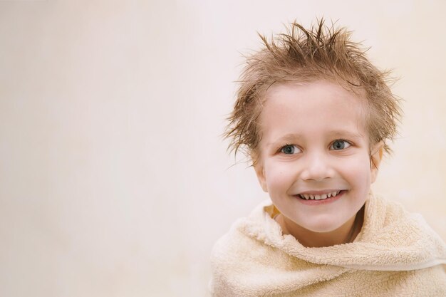 Zdjęcie mały chłopiec z mokrymi włosami nie patrzy na aparat, uśmiechnięty ząb, zawinięty w pomarańczowy ręcznik