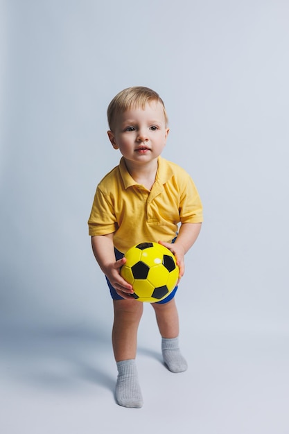 Mały chłopiec z piłką w dłoniach na białym tle dziecko jest początkującym piłkarzem sport dla dzieci Mały sportowiec Żółty i niebieski zestaw piłkarski dla dzieci