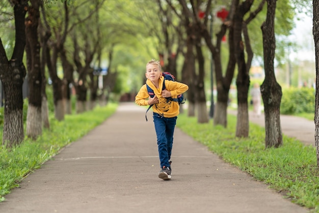 Mały chłopiec z plecakiem na ramionach biegnie z uśmiechem na twarzy i wraca do szkoły