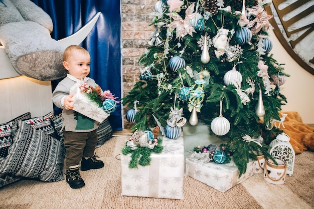 Mały chłopiec z zabawkami w pobliżu wystroju Bożego Narodzenia i choinki