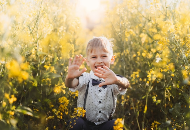 Mały chłopiec zabawy i macha rękami do kamery w przyrodzie w lecie. Słodkie urocze dziecko na polu rzepaku, bliski portret