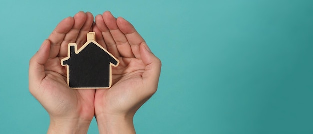 Mały drewniany dom w rękach reprezentuje koncepcje, takie jak miłość rodzinna do opieki domowej