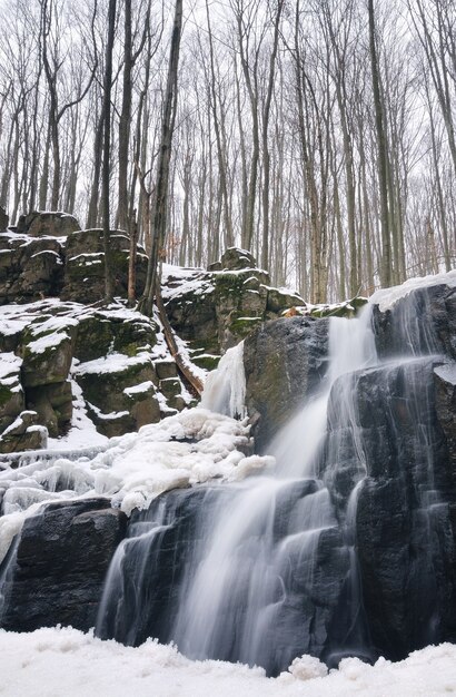 Mały górski wodospad jest pokryty śniegiem. Strumień w lesie, zimowy krajobraz, jasne tło