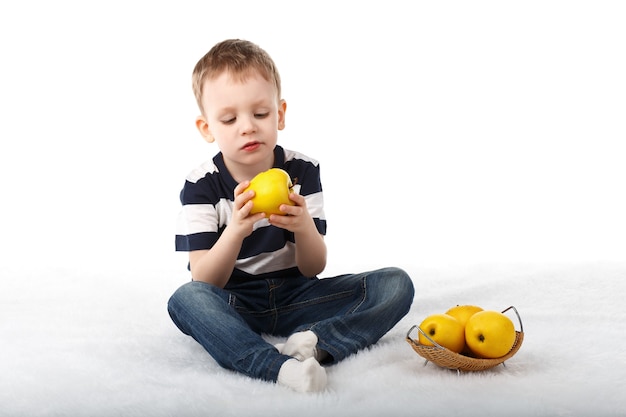 Mały ładny chłopiec jedzenie żółte jabłko i uśmiechnięty na białym tle