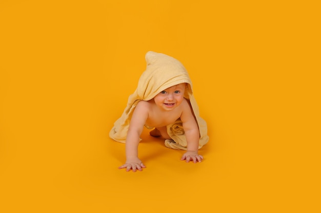 mały piękny chłopiec z niebieskim pokrytym ręcznikiem czołga się na żółtym tle studio