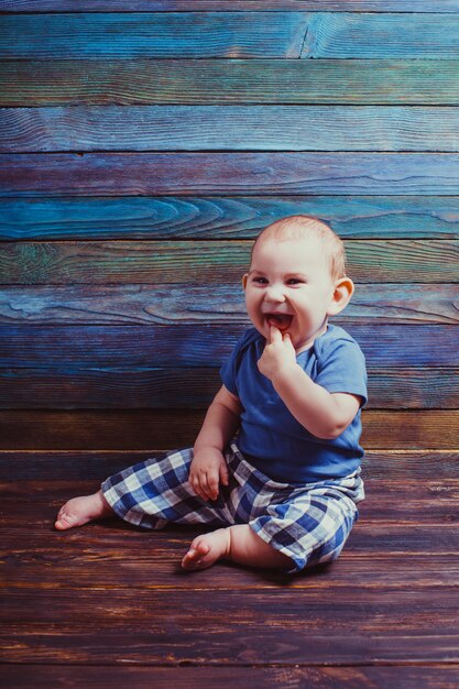 Mały radosny chłopiec z palcem w ustach na kolorowym drewnianym tle