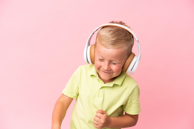 Mały rosyjski chłopiec odizolowany na różowym tle słuchający muzyki i z kciukiem do góry