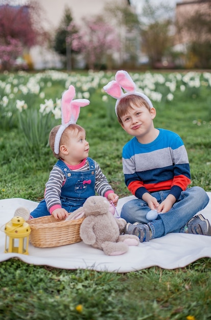 Mały śliczny chłopiec i dziewczynka siedzą na trawie w pobliżu żonkili