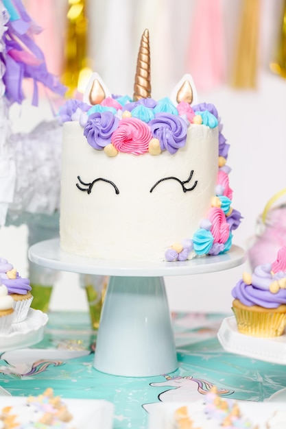 Mały stół urodzinowy dla dziewczynki z ciastem jednorożca, babeczkami i ciasteczkami cukrowymi.