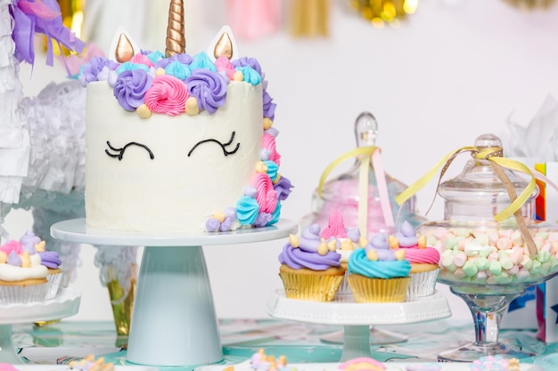 Mały stół urodzinowy dla dziewczynki z ciastem jednorożca, babeczkami i ciasteczkami cukrowymi.