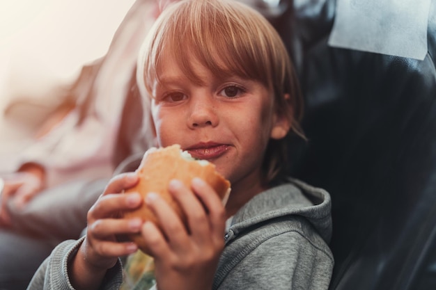 Mały, Szczery Chłopczyk W Wieku Pięciu Lat Je Burgera Lub Kanapkę Siedząc W Samolocie W Samolocie Lecąc Z Lotniska Dzieci Gryzą Dziecko W Samolocie Jedząc Obiad Lub Kolację