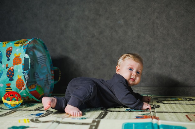 Mały sześciomiesięczny chłopiec uczy się pełzać po dywanie, dziecko pełza i trzyma głowę, dziecko w szarych ubraniach.