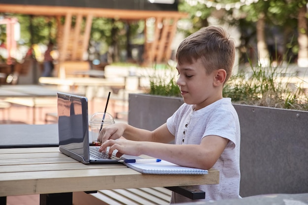 Mały uczeń siedzi na świeżym powietrzu na klawiaturze laptopa