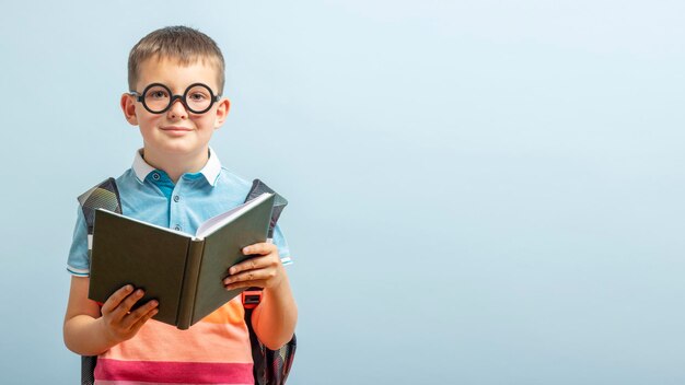 Mały uczennik w okularach czyta książkę na niebieskim tle