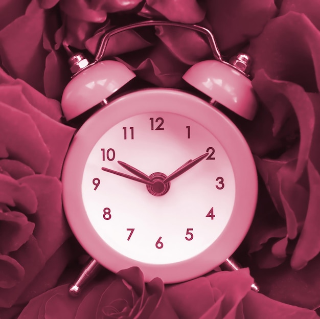 Mały, uroczy budzik otoczony motywem różyczek stonowanych w kolorze viva magenta roku