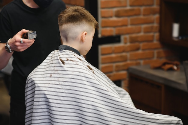 Mały uroczy chłopczyk siedzi u fryzjera u stylisty, uczeń strzyże włosy w salonie piękności, dziecko u fryzjera, krótka męska fryzura.