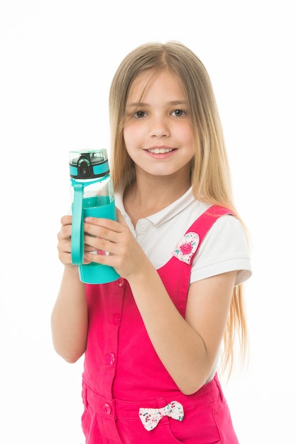 Mały uśmiech dziewczyny z plastikowej butelki na białym tle. Szczęśliwe dziecko w różowym kombinezonie trzymać butelkę wody. Woda pitna dla zdrowia. Pragnienie i odwodnienie. Aktywność i energia w dzieciństwie.