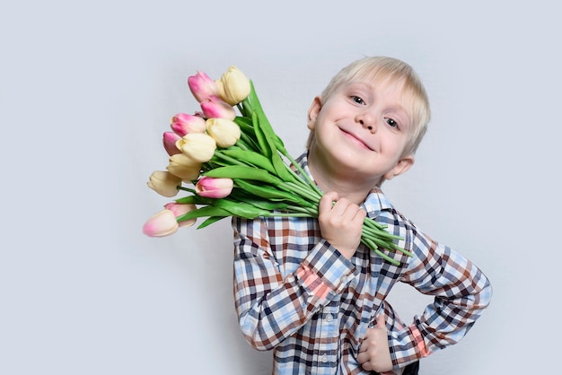 Mały uśmiechnięty blond chłopiec trzyma bukiet tulipanów.