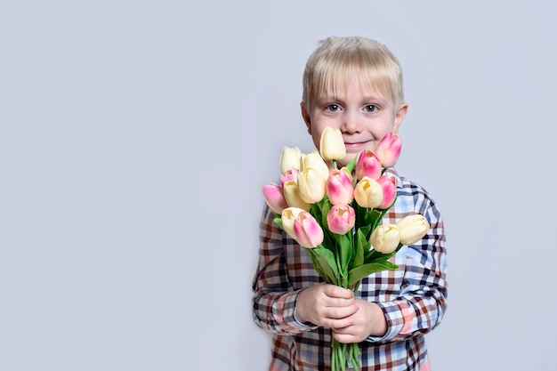 Mały uśmiechnięty blond chłopiec trzyma bukiet tulipanów.