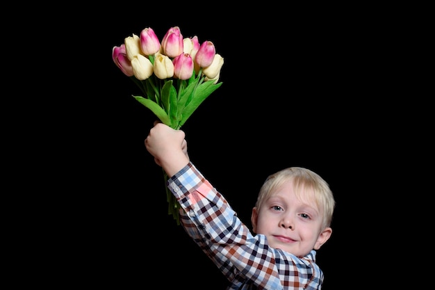 Mały uśmiechnięty blond chłopiec z bukietem tulipanów. Koncepcja dzień matki. Portret. Izoluj na czarnej ścianie.