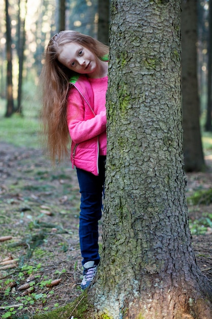 Małych dziewczynek spojrzenia zza drzewa w lesie