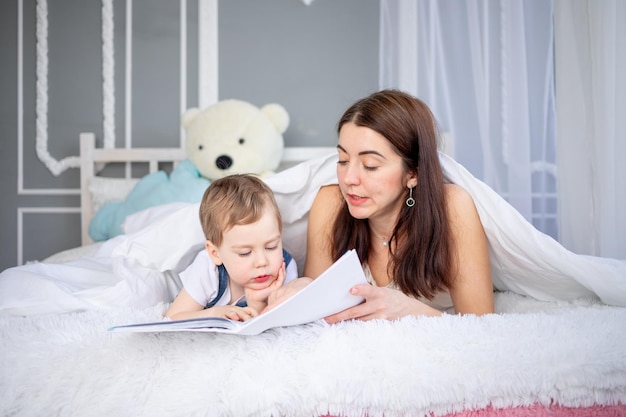 Mama czyta dziecku książkę lub uczy go w domu na łóżku Szczęśliwa kochająca rodzina Mama i syn