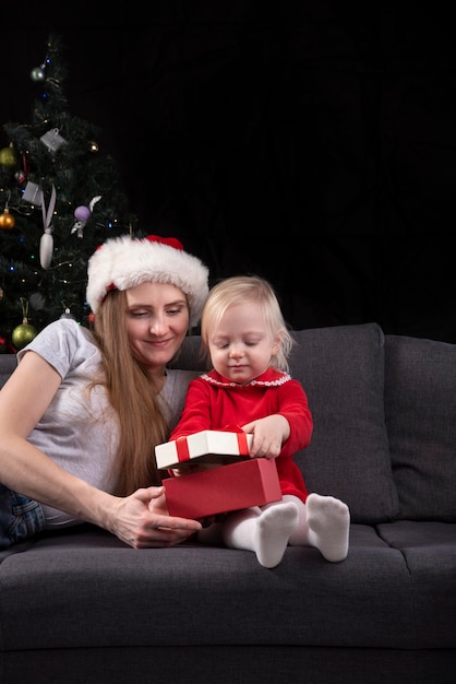 Mama I Córeczka Rozpakowują Prezenty Sylwestrowe Na Kanapie W Domu Na Tle Choinki. Rama Pionowa