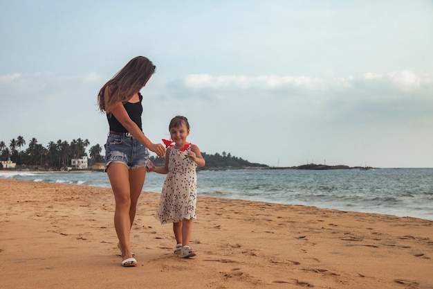 Mama i córeczka z kwiatami razem spacery po tropikalnej piaszczystej plaży na tle oceanu