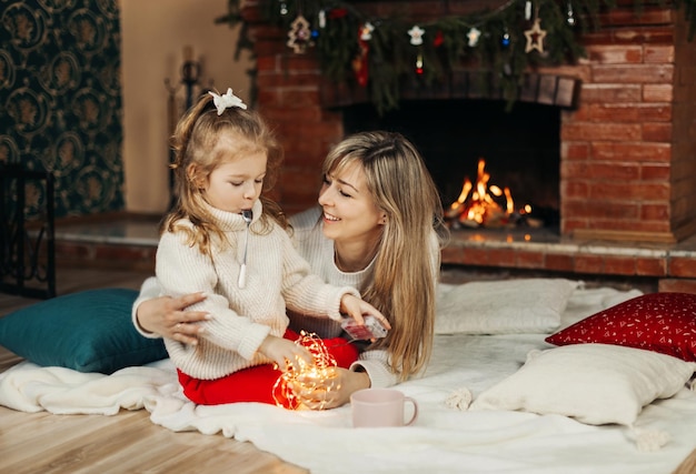 Mama i córka bawią się gwiazdkami świątecznymi na podłodze przy kominku.