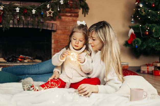 Mama i córka bawią się gwiazdkami świątecznymi na podłodze przy kominku.