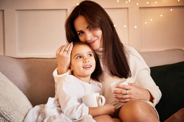 Mama i córka rozmawiają na kanapie w salonie urządzonym na Boże Narodzenie. Młoda szczęśliwa rodzina świętuje Boże Narodzenie. Przytulne Święta