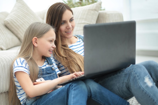 Mama i córka siedzą na dywanie w salonie i korzystają z laptopazdjęcie z miejscem na kopię