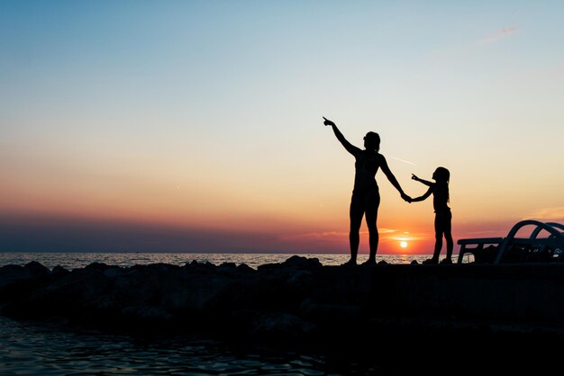 Mama i córka spędzają czas nad morzem na tle zachodzącego słońca