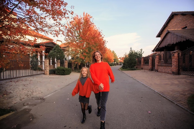 Mama i córka w pomarańczowych sweterkach bawią się na spacerze po ulicy w pobliżu wiejskich domów