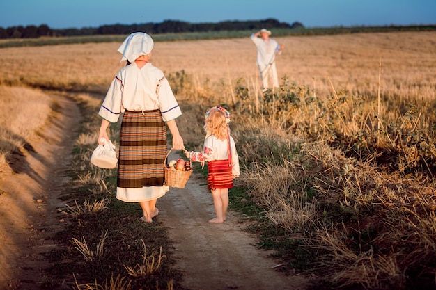 Mama i córka w strojach ludowych niosą tatę do jedzenia w terenie