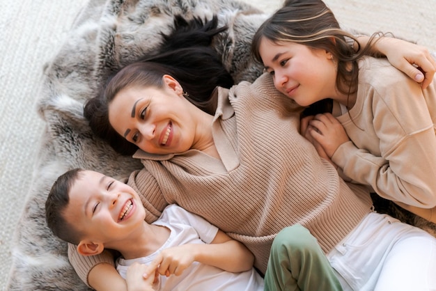 Mama i dzieci leżą na łóżku w urządzonej sypialni i śmieją się z koncepcją zimowych wakacji z rodziną