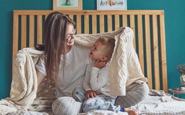 Mama i dziecko bawią się w sypialni na łóżku, bawią się pod kocem