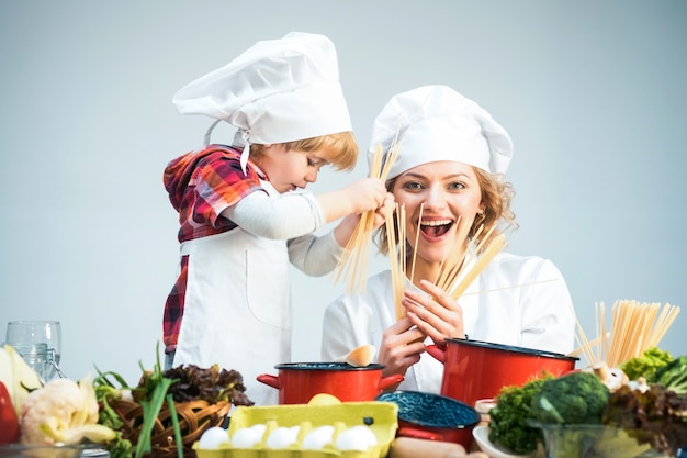 Zdjęcie mama i dziecko razem gotują spaghetti z uśmiechniętą twarzą matka uczy syna gotować