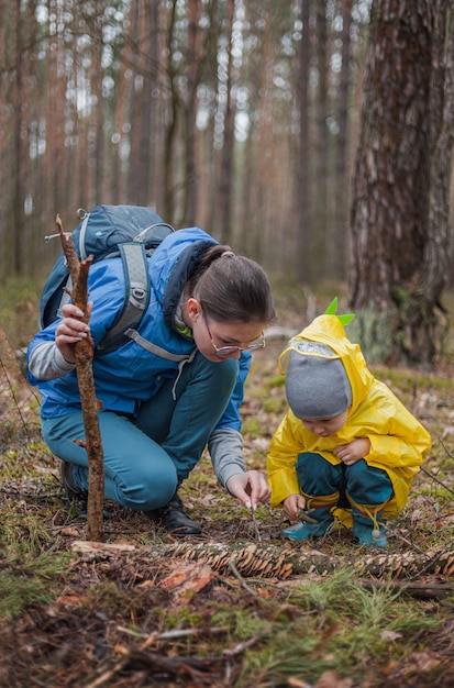 Mama i dziecko spacerują razem po lesie po deszczu w płaszczach przeciwdeszczowych, patrząc na grzyby na zwalonym drzewie i rozmawiając