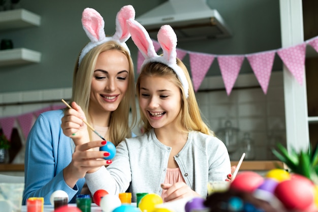 Mama i jej córka malują w kuchni jajko wielkanocne. Wesołych Świąt Wielkanocnych.