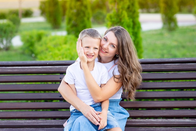 Mama i jej synek w parku na ławce latem bawią się przytulając, śmiejąc się i bawiąc