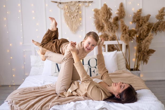 Mama i mały chłopiec bawią się w przytulanie i robią samolot w domu na łóżku w naturalnych odcieniach brązu szczęśliwa rodzina z małym dzieckiem bawi się razem