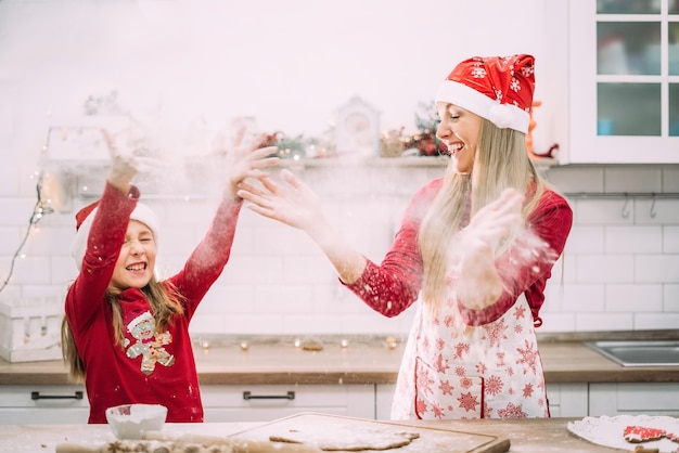 Mama I Nastoletnia Córka Bawią Się W Kuchni Mąką, Czerwonymi Swetrami I Czapką Mikołaja.