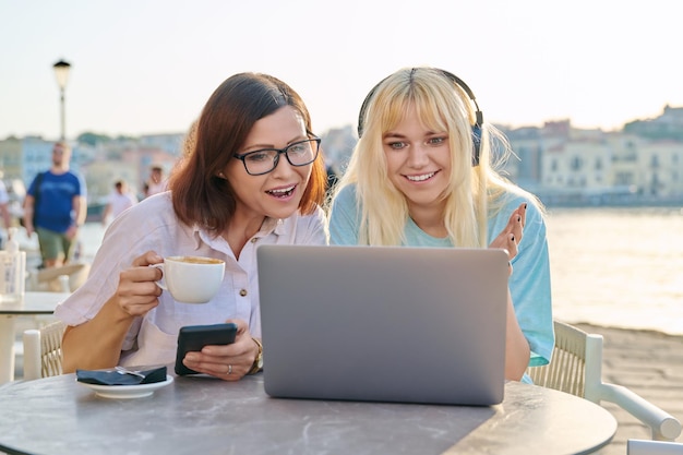 Mama i nastoletnia córka patrzą razem na laptopa siedząc w kawiarni na świeżym powietrzu