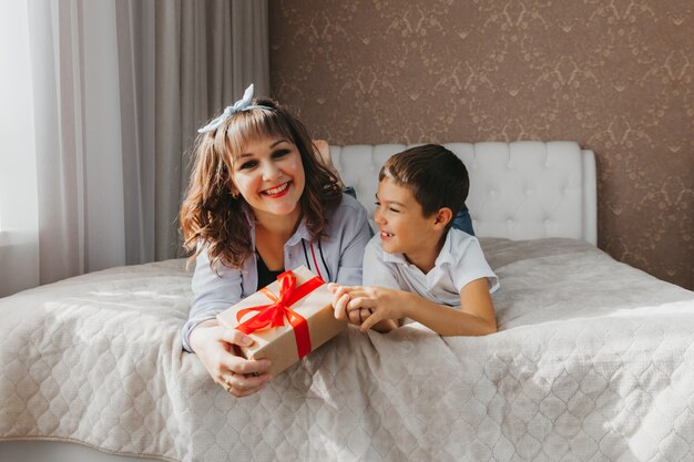 Mama i syn leżą na łóżku. dziecko daje mamie prezent na dzień matki.