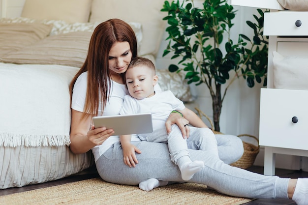 Zdjęcie mama i syn siedzą na podłodze w pokoju i razem patrzą na cyfrowy tablet