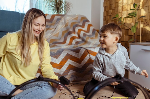 Mama i synek bawią się w wyścigi na dywanie w domu, bawią się i przytulają Samotna matka wychowuje syna, bawiąc się samochodami