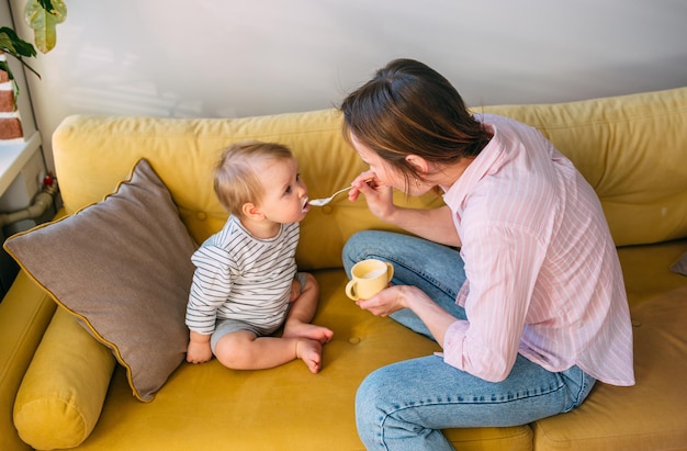 Mama karmi małe dziecko w domu jogurtem z koncepcji rodziny łyżek